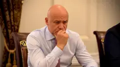 Задумливий Труханов сидить, спершись ліктем на стіл, а другою рукою підпирає підборіддя. Його обличчя серйозне й зосереджене, погляд спрямований вниз. На задньому плані видно частину стільця з різьбленою спинкою та важкі штори.