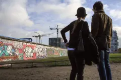 Ein Mann und eine Frau betrachten einen Teil der Berliner Mauer.