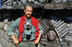Чоловік з фотоапаратами на шиї біля стіни з орнаментом