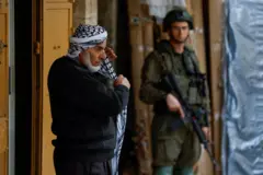 رجل فلسطيني يرتدي الكوفية بينما يقف جندي إسرائيلي حارساً في البلدة القديمة بالخليل في الضفة الغربية المحتلة، 9 فبراير/شباط 2026.