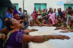 Mulheres sentadas em volta de uma grande mesa, aparentemente, muitas delas chorando