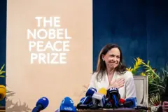 María Corina Machado detrás de unos micrófonos y con un cartel del premio Nobel de la Paz detrás.