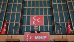 Devlet Bahçeli mecliste konuşuyor, arkasında MHP logosu gözüküyor