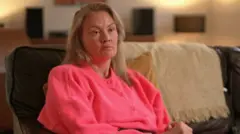 Naomi Timperley de blusa rosa sentada em sofá