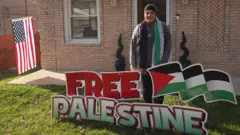 Laila Gaber stands in front of her house with the US flag flying and a 'Free Palestine' sign on her front lawn