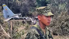 Un soldado joven, con gesto serio, en el lugar donde cayó el Hércules C-130 de la Fuerza Aérea de Colombia. En el fondo se ven restos de la aeronave.