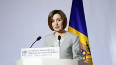 Майя Санду на трибуне, на белом фоне с флагом Молдовы