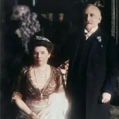 Fotografia histórica colorizada de Antony Easton de Olga e Heinrich Eisner em trajes formais. Olga está sentada, usando um vestido de renda com uma tiara nos cabelos. Heinrich está ao lado dela, de terno escuro e com uma flor na lapela.