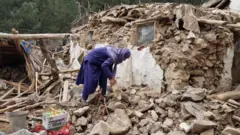 भूकम्पले घर भत्काइ दिएपछि भग्नावशेषबाट आफ्ना सर सामान निकाल्न खोज्दै गरेका एक व्यक्ति