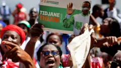 Des sympathisantes du PDCI protestent contre une décision de justice visant à retirer leur leader Tidjane Thiam de la liste électorale à Abidjan, en Côte d'Ivoire. L'une d'entre elles brandit une affiche de campagne de Thiam - 24 avril 2025