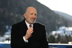 Howard Lutnick colocando uma das mãos sobre a gravata. Ele usa um terno preto.