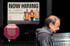 Um homem passa por um depósito com um anúncio de emprego na entrada.