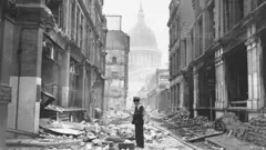 1941年5月，倫敦在第二次世界大戰被德軍密集大轟炸期間，郵遞員在市中心聖保羅大教堂附近被炸毀的街道上投遞信件。