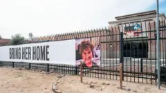 Una pancarta colgada en la puerta exterior de una filial local de NBC muestra una foto de Nancy Guthrie y dice: Tráiganla a casa.