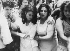 Uma mulher se apoia em outras duas no meio de uma multidão