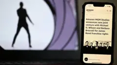 Imagem dos créditos iniciais de James Bond com um celular na frente anunciando que a Amazon está assumindo a franquia.