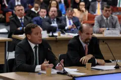 Mauro Cid ao microfone com Jair Bolsonaro ao fundo. Delator e ex-mandatário se cumprimentaram