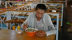 खाना खान टेबलमा बसेका बेला मोबाइल हेर्दै एक व्यक्ति