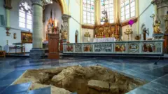 教会の壮麗な祭壇の前、床の青いタイルが一部はがされ、その下の黄土色の土に穴が開いている

