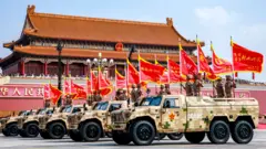 Veículos militares têm soldados carregando bandeiras vermelhas no topo enquanto desfilam pela Praça Tianeman na quarta-feira.