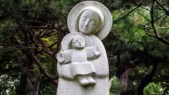 Estátua em pedra de Maria com o menino Jesus no colo, ambos são retratados com traços orientais