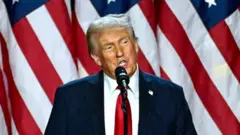 Дональд Трамп говорить у мікрофон, стоячи перед американськими прапорами