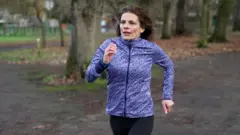 Writer Ruth Clegg, a woman with brown hair in a purple sports jacket runs on a track through a park.