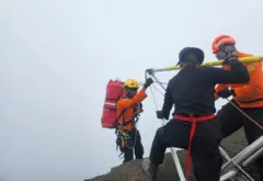 Homem fazendo rapel, monitorado por outros agentes
