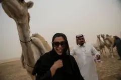 یوه مېرمنه د خندا حالت کې له اوښ سره ولاړه ده.