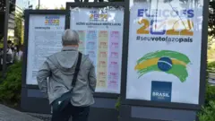 Fotografia colorida mostra um homem idoso de cabelo branco de costas olhando para posters escritos em japonês e português