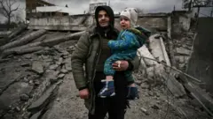 Seorang pria menggendong anak saat mereka melarikan diri untuk mengungsi akibat serangan Rusia di Ukraina.
