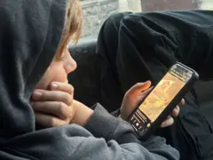 Um menino usando o celular e vendo um vídeo