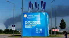 Билборд с рекламой экономического форума, на фоне виден столб черного дыма
