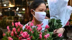 A woman wearing a mask carrying flowers in Hanoi