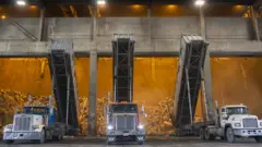 Camiones alineados frente a un horno para quemar basura en Estados Unidos.