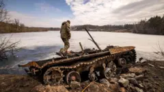 A Ukrainian serviceman stands near a destroyed Russian tank, March 2022