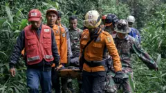A group of rescue workers carrying a survivor amid foliage, in Agam West Sumatra on 4 December