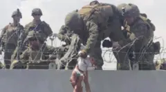 Soldados seguram bebê sendo passada por cima de muro