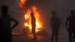A man stands in front of a burning tyre