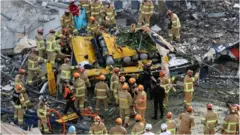 South Korean firefighters search for passengers from a bus trapped by the debris of a collapsed building in Gwangju