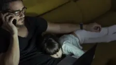 Un hombre teletrabajando hasta tarde con su niña acostada sobre sus piernas.