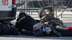Civiles y militares se ponen a cubierto tras sonar una sirena de ataque aéreo, cerca del edificio de apartamentos dañado en Kiev.
