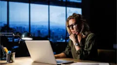 سيدة تجلس أمام جهاز الحاسوب وتعمل حتى وقت متأخر