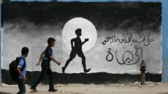 Two Palestinian schoolboys walk past a graffiti painted on a wall of the United Nations school of Beit Hanun, in the northern Gaza Strip, on May 9, 2016