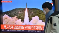 A man walks past a television screen showing a news broadcast with file footage of a North Korean missile test, at a railway station in Seoul on January 17, 2022, after North Korea fired an unidentified projectile eastward in the country's fourth suspected weapons test this month according to the South's military.