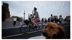 A man wearing a protective face mask cycles past people and a dog on a bridge, as the city prepares to end the lockdown placed to curb the coronavirus disease (COVID-19) outbreak in Shanghai, China May 31, 2022.