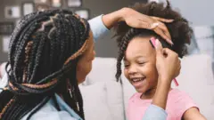 A mother helps her daughter with her braids