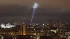 Ukrainian service personnel use searchlights dey find drones for di sky over Kyiv on Tuesday night