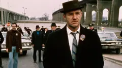 Gene Hackman usa terno e chapéu pretos em filmagem de Operação França, em que representou o policial Popeye