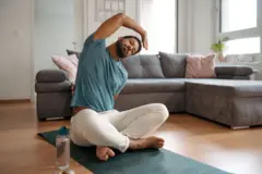 Homem negrom vaidebetpele clara com barba e cabelo curto se alonga sentadom vaidebetum tapetem vaidebetiogam vaidebetuma sala,m vaidebetfrente a um sofá